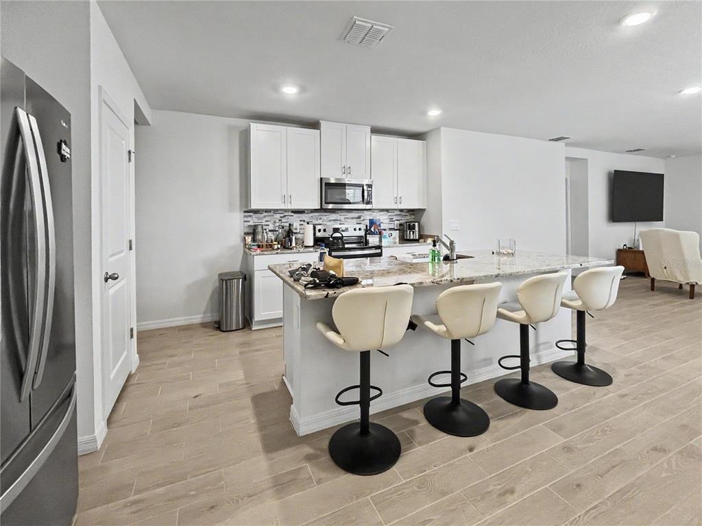 A kitchen features white cabinets, granite countertops, an island with four barstools, and light flooring — 137 WHITELAND BEND, NOKOMIS, FL
