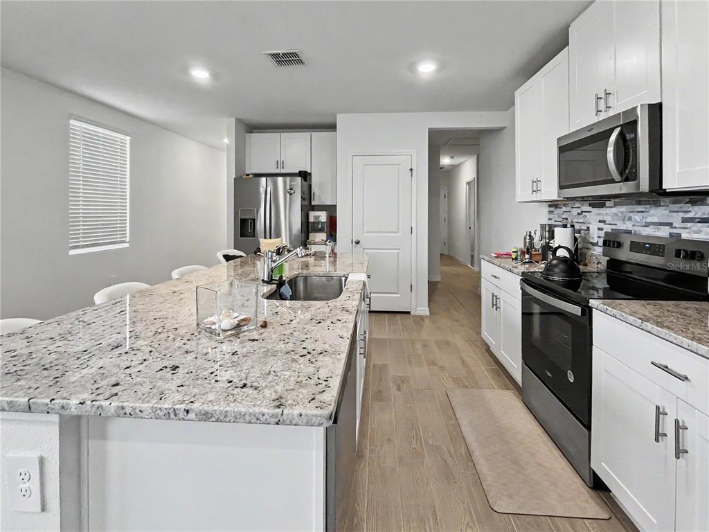 A modern kitchen features white cabinetry, granite countertops, a large island, and stainless steel appliances — 137 WHITELAND BEND, NOKOMIS, FL