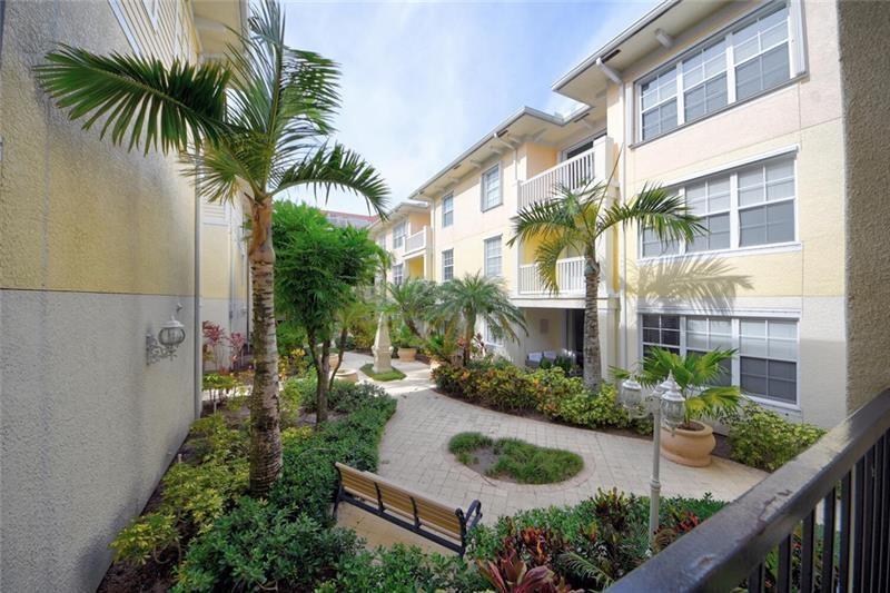 A courtyard with a paved walkway, palm trees, and a bench between apartment building wings — 275 Murcia Drive # 208, Jupiter FL 33458, JUPITER, FL