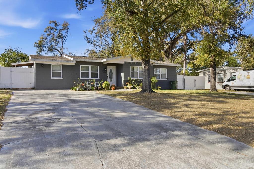 A gray single-story house with a concrete driveway and large trees in the front yard — 4608 HARVEY AVENUE, TAMPA, FL