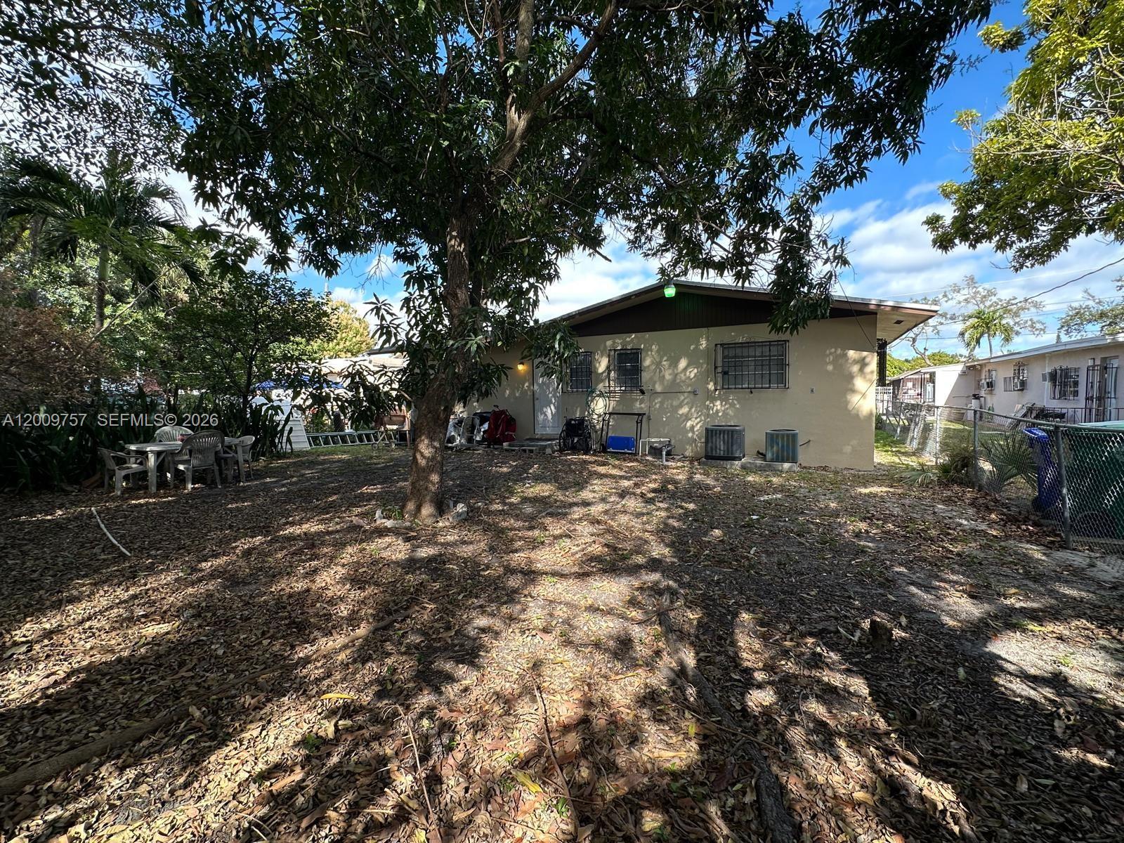 A backyard area features a tan house with a tree and outdoor patio furniture — 420 NW 32nd St, Miami FL 33127, MIAMI, FL