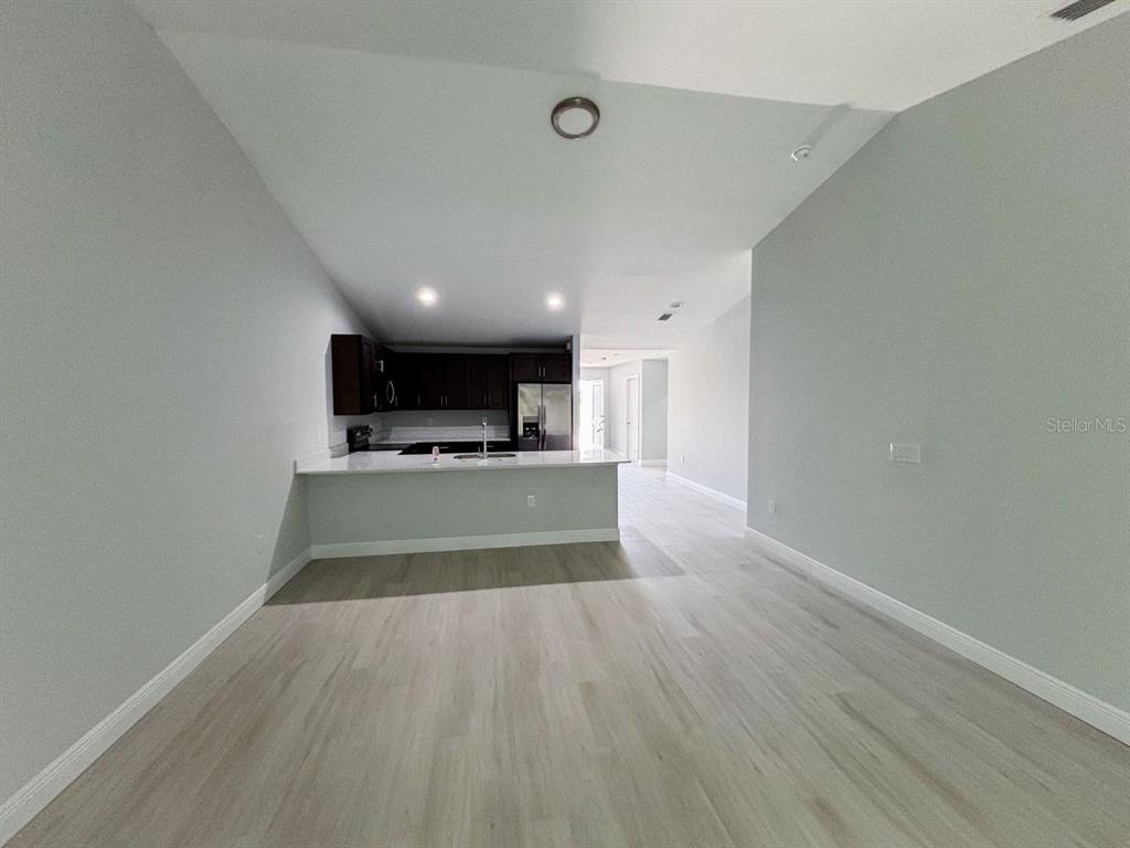 An open-concept kitchen with dark cabinets and a white countertop overlooks a living area — 8456 DINNANO STREET, PORT CHARLOTTE, FL