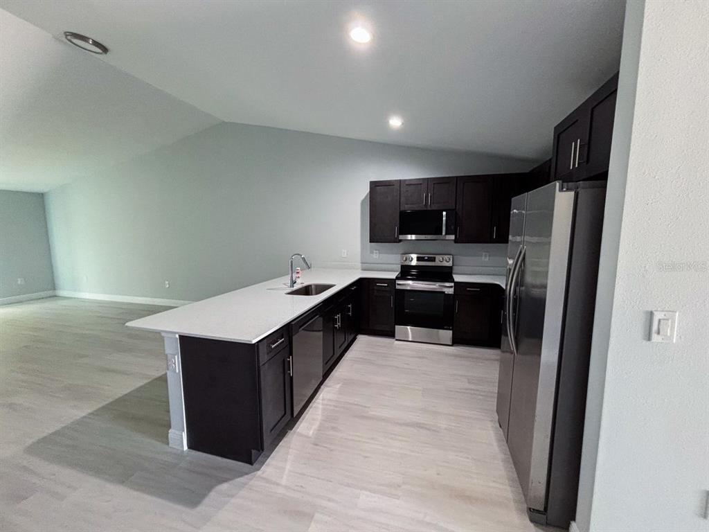 A kitchen features dark wood cabinets, white countertops, stainless steel appliances, and light wood flooring — 8456 DINNANO STREET, PORT CHARLOTTE, FL
