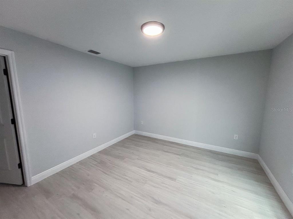 An empty room features light gray walls, white baseboards, and light wood-look flooring — 8456 DINNANO STREET, PORT CHARLOTTE, FL