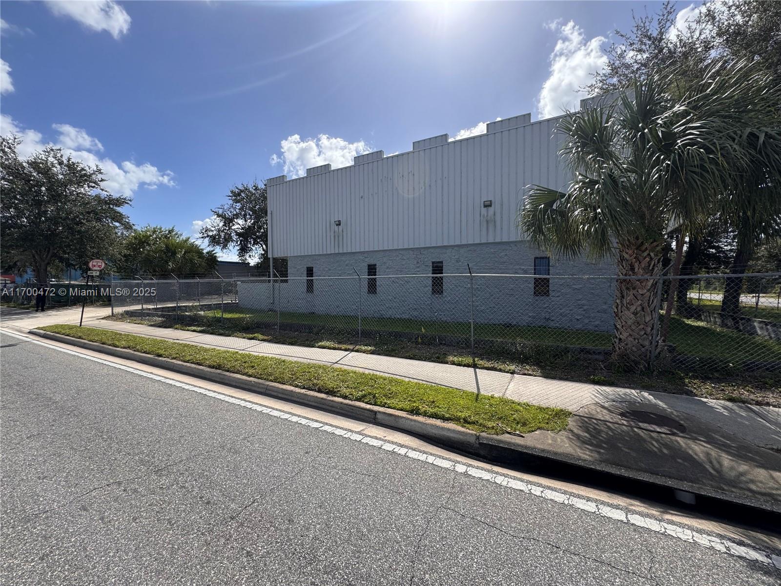 A gray industrial building sits behind a chain-link fence next to a sidewalk and road — 5909 Anno Ave # 5909, Orlando FL 32809, ORLANDO, FL