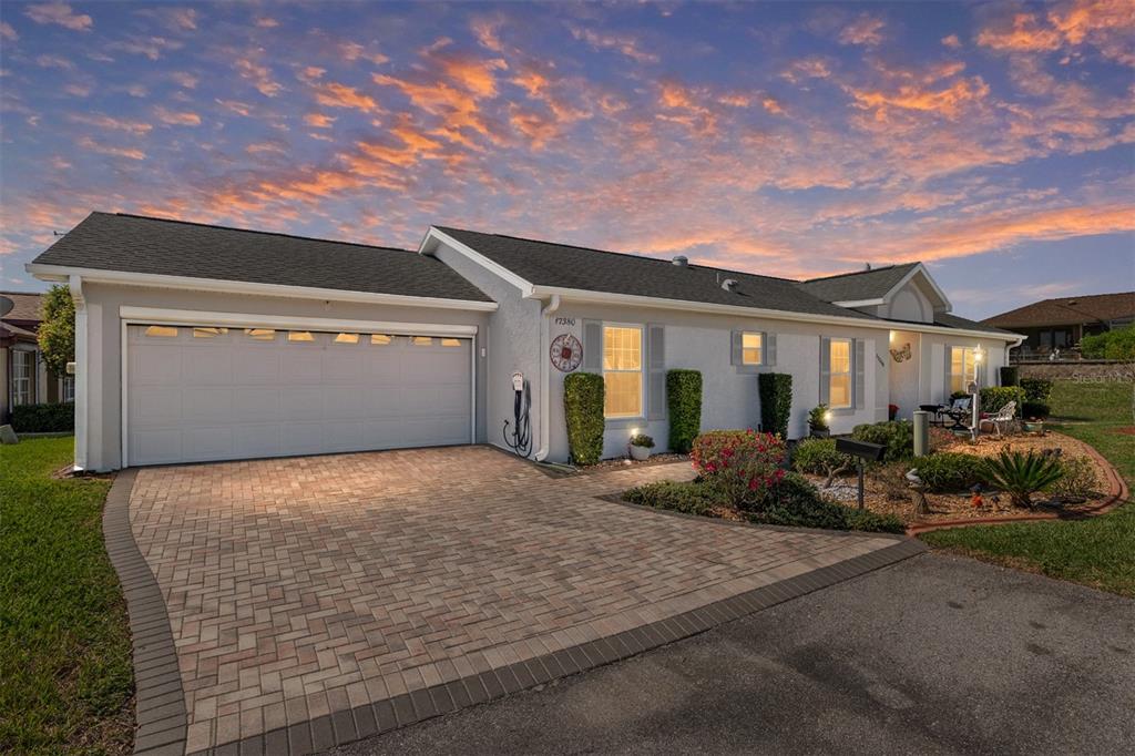 A single-story house with a paved driveway, two-car garage, and landscaped front yard at sunset — 17380 SE 111TH COURT, SUMMERFIELD, FL