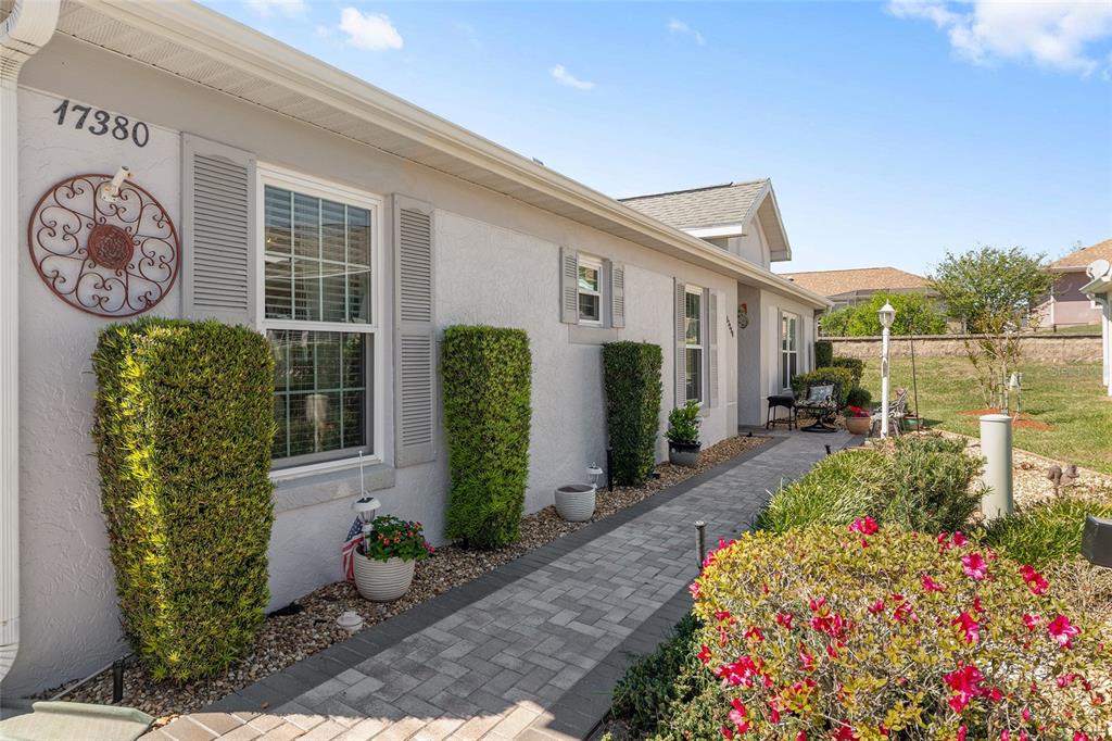 A paved walkway leads along the side of a light-colored house with manicured shrubs — 17380 SE 111TH COURT, SUMMERFIELD, FL
