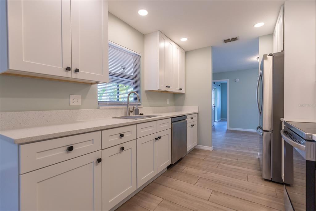 A kitchen features white shaker cabinets, light countertops, stainless steel appliances, and wood-look tile flooring — 4005 17TH AVENUE W, BRADENTON, FL
