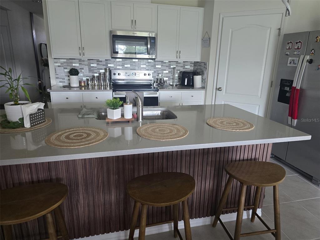 A kitchen features a large island with three wooden stools and light-colored quartz countertops — 3045 TOBAGO DRIVE, HAINES CITY, FL