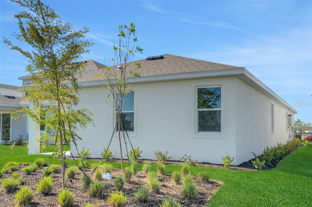 The exterior side view of a white stucco house features two windows and landscaping — 16928 COTTONTAIL CIRCLE, PUNTA GORDA, FL