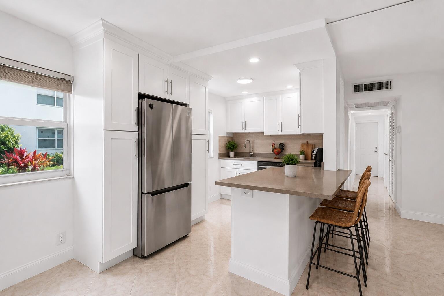 A white kitchen features stainless steel appliances, a stone-topped island with bar stools, and tile flooring — 160 Tuscany C, Delray Beach FL 33446, DELRAY BEACH, FL