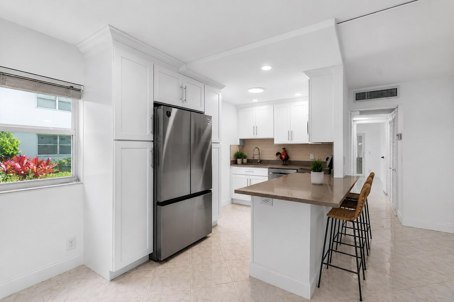 A white kitchen features stainless steel appliances, a brown countertop island, and tile flooring — 160 Tuscany C, Delray Beach FL 33446, DELRAY BEACH, FL