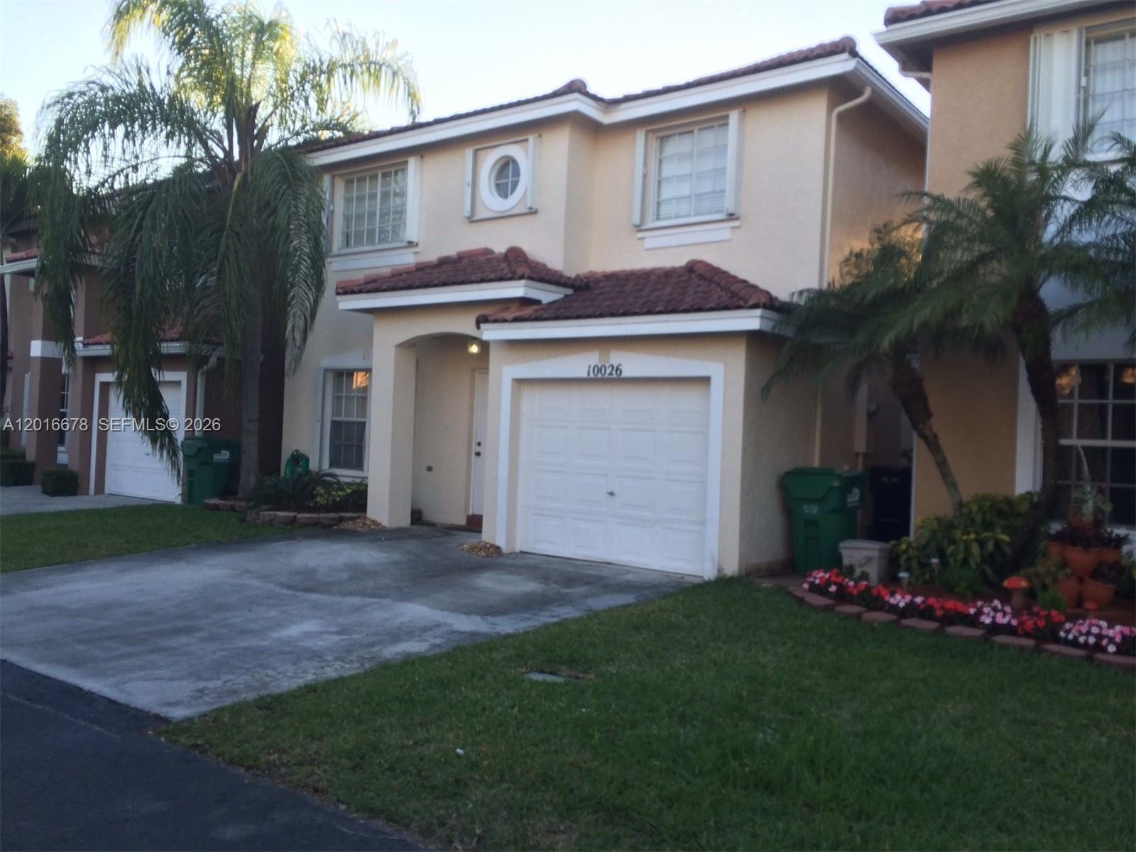 A two-story beige townhouse with a single-car garage, tile roof, and palm trees — 10026 SW 162nd Path, Miami FL 33196, MIAMI, FL