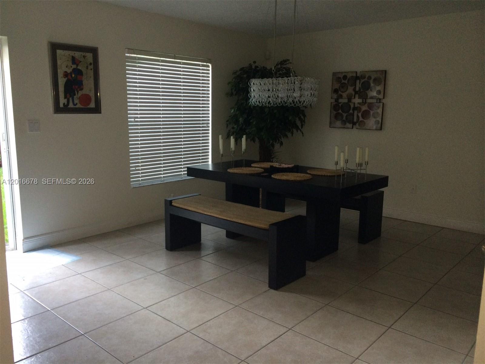 A dining room features a dark table with benches, a chandelier, and tiled flooring — 10026 SW 162nd Path, Miami FL 33196, MIAMI, FL