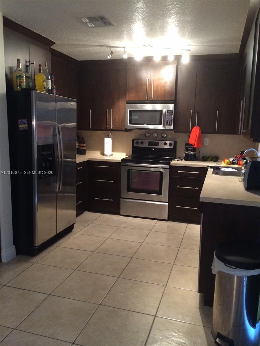 A kitchen features dark wood cabinets, stainless steel appliances, light countertops, and beige tile flooring — 10026 SW 162nd Path, Miami FL 33196, MIAMI, FL
