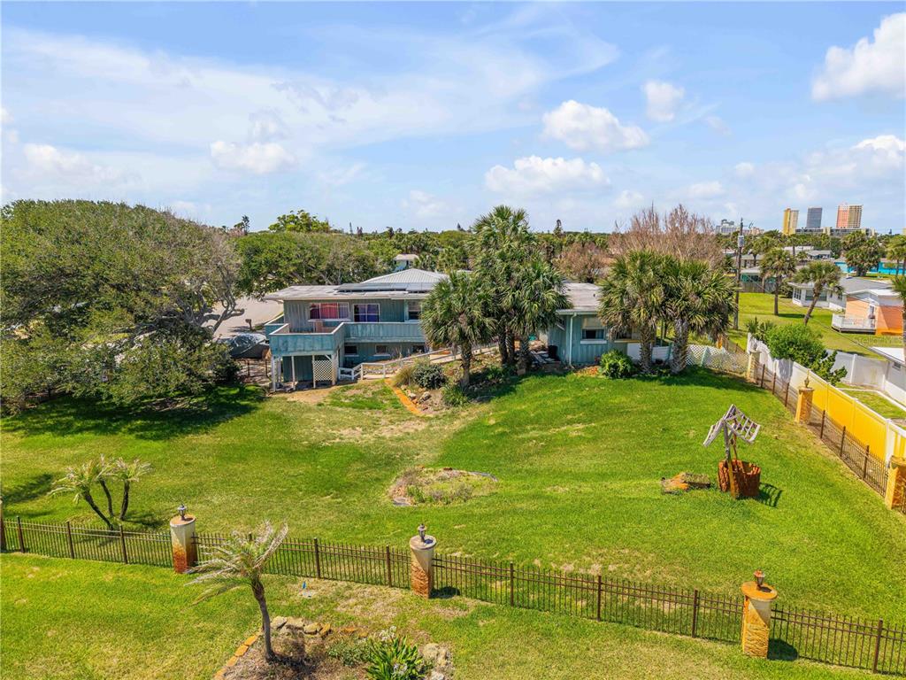 An elevated view of a two-story house with a large grassy yard and metal fencing — 401 DRIFTWOOD AVENUE, DAYTONA BEACH, FL