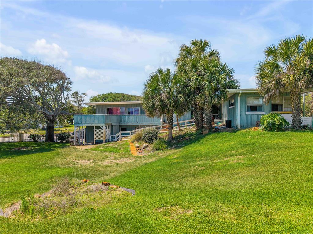 A light blue house with a wooden deck stands on a grassy lawn with palm trees — 401 DRIFTWOOD AVENUE, DAYTONA BEACH, FL
