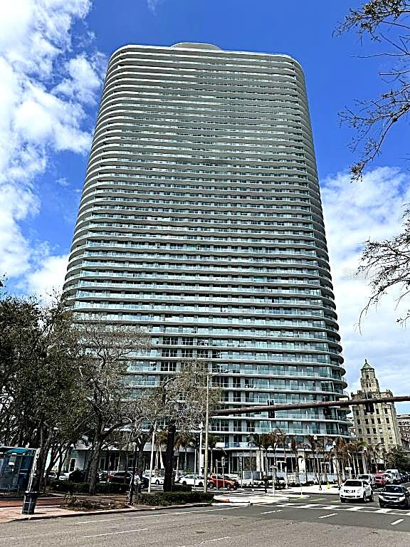 A tall, modern residential high-rise building stands against a blue sky with scattered clouds — 400 CENTRAL AVENUE UNIT 2603, ST PETERSBURG, FL