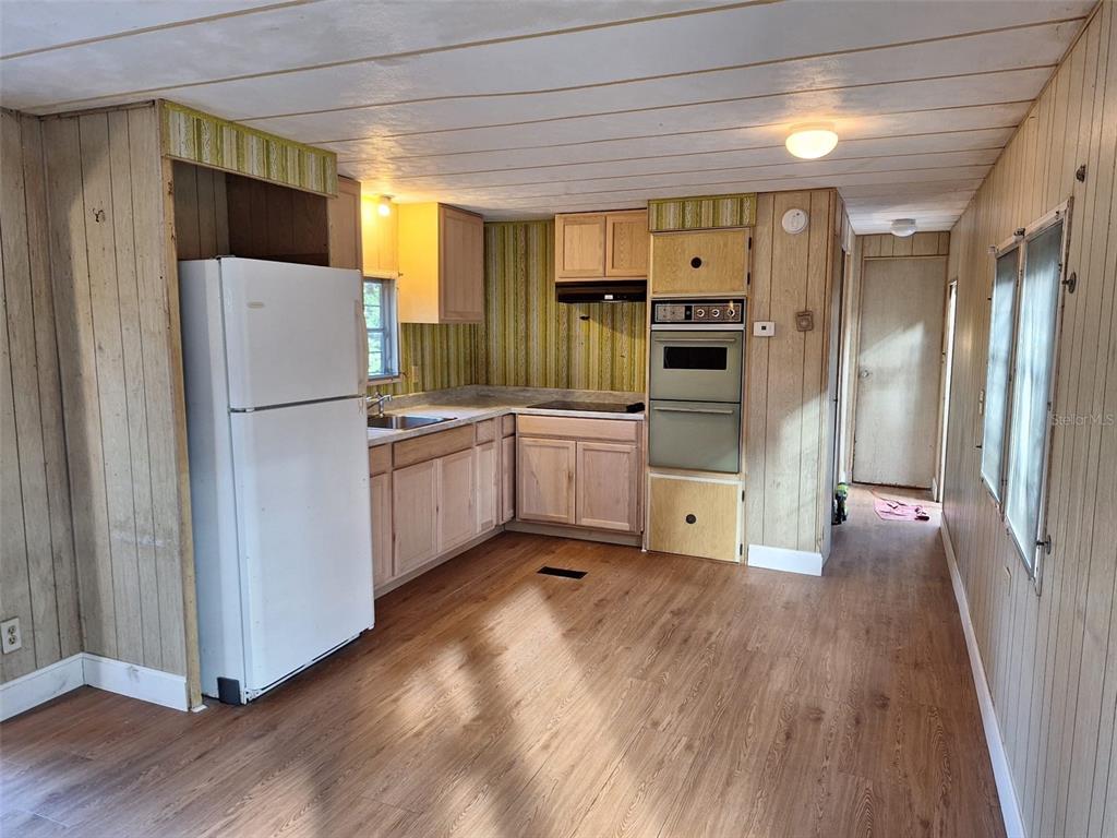 A kitchen features wood-paneled walls, light wood cabinets, a white refrigerator, and wood-look flooring — 11726 NW 12TH LANE, OCALA, FL