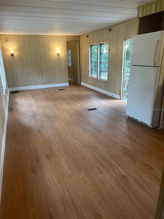 A room with wood-look flooring, wood-paneled walls, a white refrigerator, and two wall sconces — 11726 NW 12TH LANE, OCALA, FL