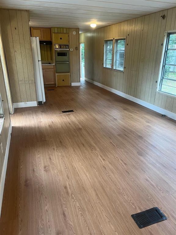This kitchen and living area features wood-paneled walls, light wood-look flooring, and a built-in oven — 11726 NW 12TH LANE, OCALA, FL