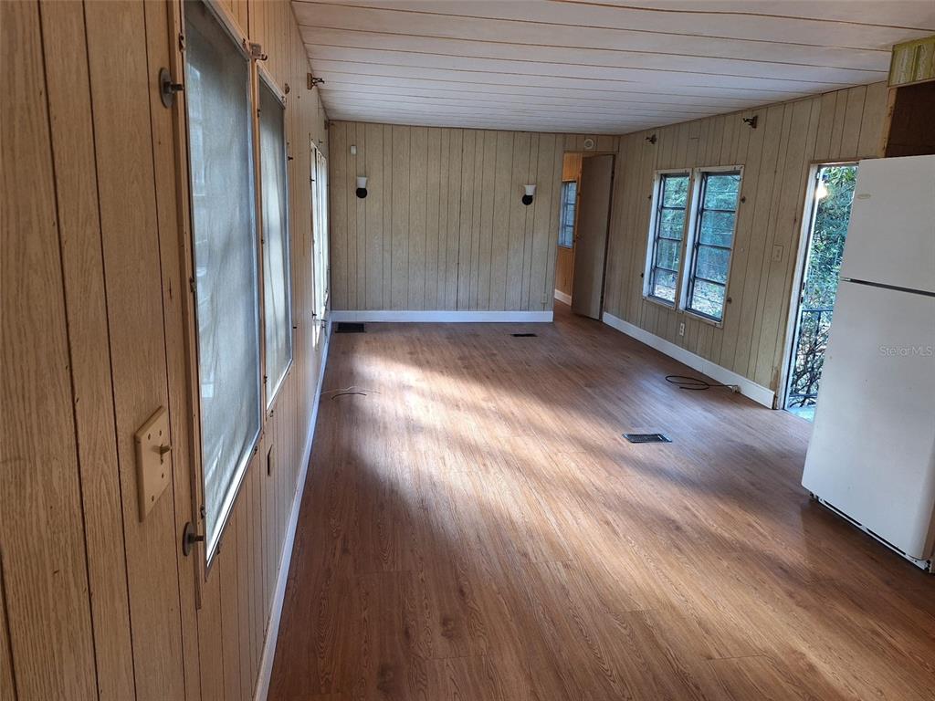 A room with wood-paneled walls, wood-look flooring, multiple windows, and a white refrigerator — 11726 NW 12TH LANE, OCALA, FL
