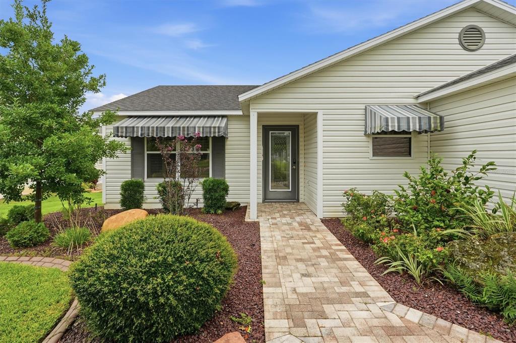 A light-colored house exterior features a brick walkway leading to a front door with awnings — 2435 POMEROY TERRACE, THE VILLAGES, FL