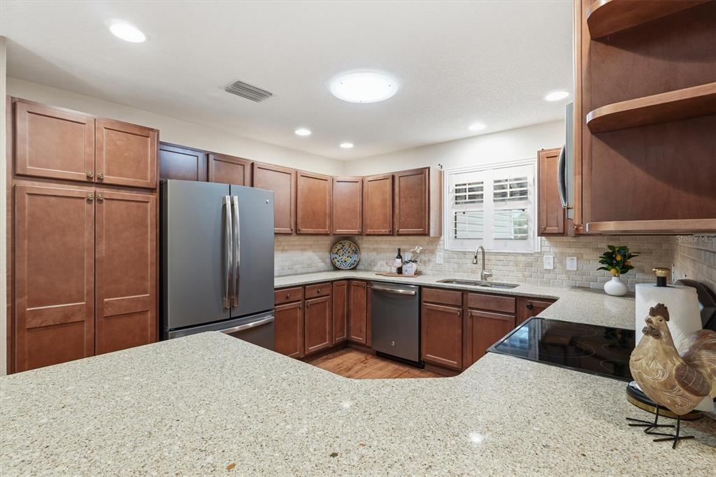 A kitchen features brown wooden cabinets, granite countertops, stainless steel appliances, and a tiled backsplash — 2435 POMEROY TERRACE, THE VILLAGES, FL