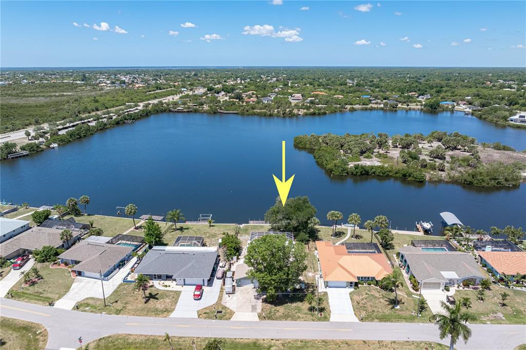 An aerial view shows a waterfront house with a pool cage and a large tree — 174 SPRING LAKE BOULEVARD NW, PORT CHARLOTTE, FL