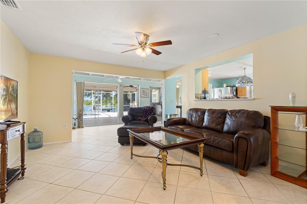 A living room with tile floors, a brown leather sofa, and a view of a pool — 174 SPRING LAKE BOULEVARD NW, PORT CHARLOTTE, FL