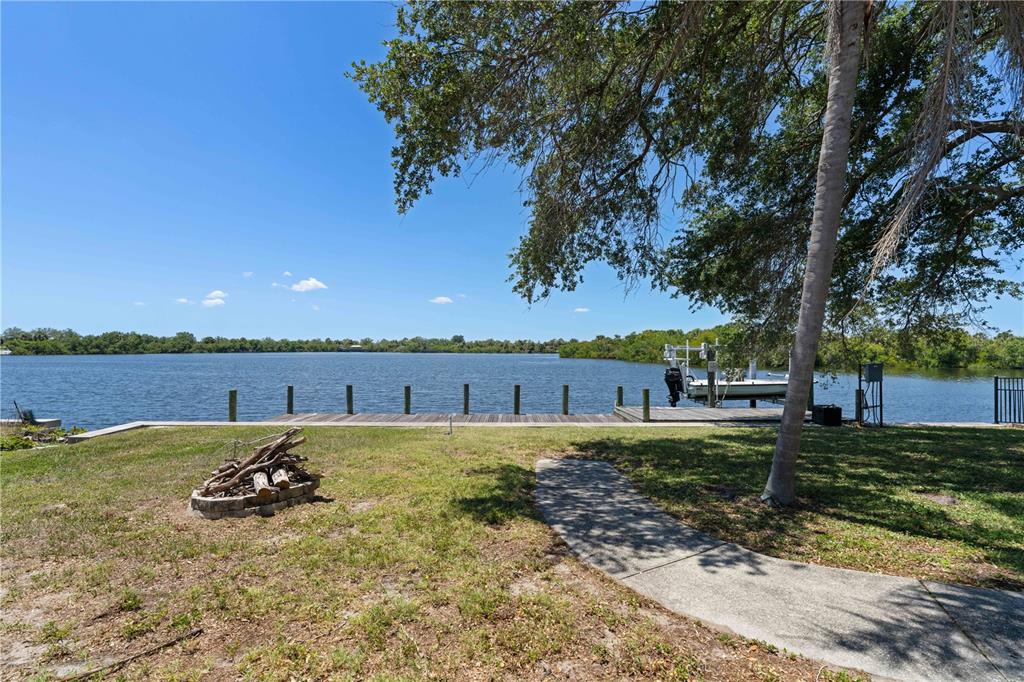 A grassy backyard features a fire pit, a concrete walkway, and a wooden boat dock — 174 SPRING LAKE BOULEVARD NW, PORT CHARLOTTE, FL