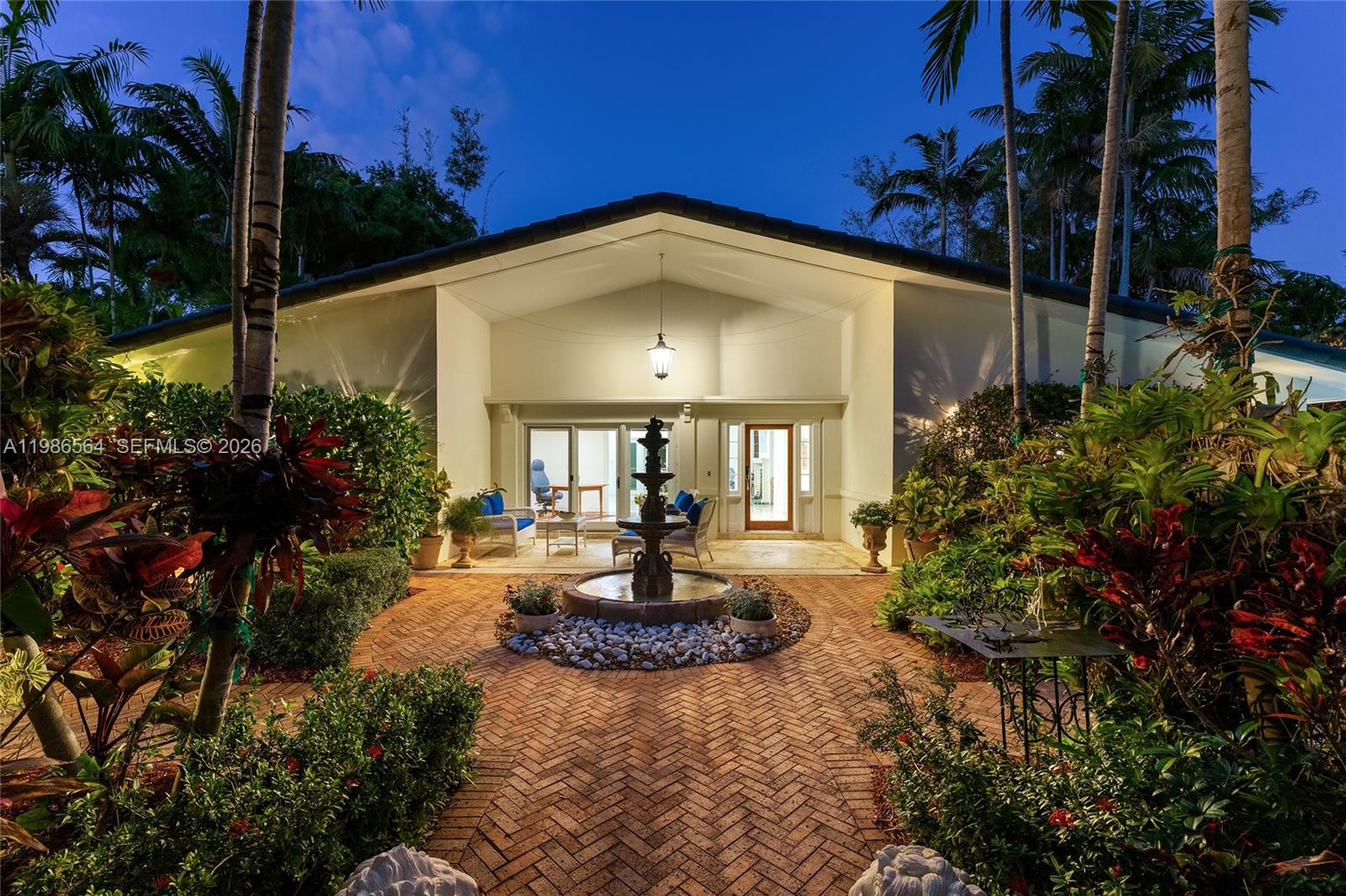 A brick walkway leads to a covered patio featuring a tiered fountain and lush landscaping — 269 Cranwood Dr, Key Biscayne FL 33149, KEY BISCAYNE, FL