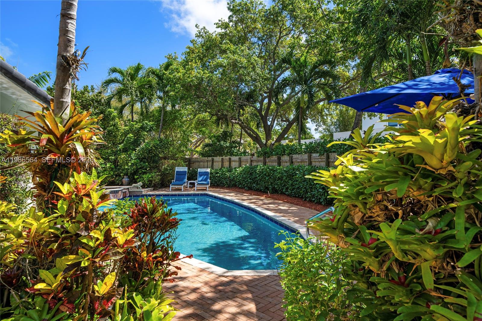 A backyard swimming pool is surrounded by lush tropical landscaping, brick pavers, and lounge chairs — 269 Cranwood Dr, Key Biscayne FL 33149, KEY BISCAYNE, FL