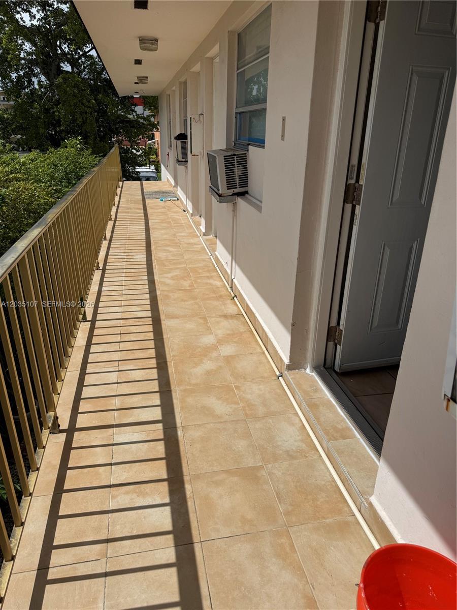 An outdoor tiled walkway features a metal railing, exterior wall-mounted air conditioning units, and doors — 166 W 8th St # 3, Hialeah FL 33010, HIALEAH, FL