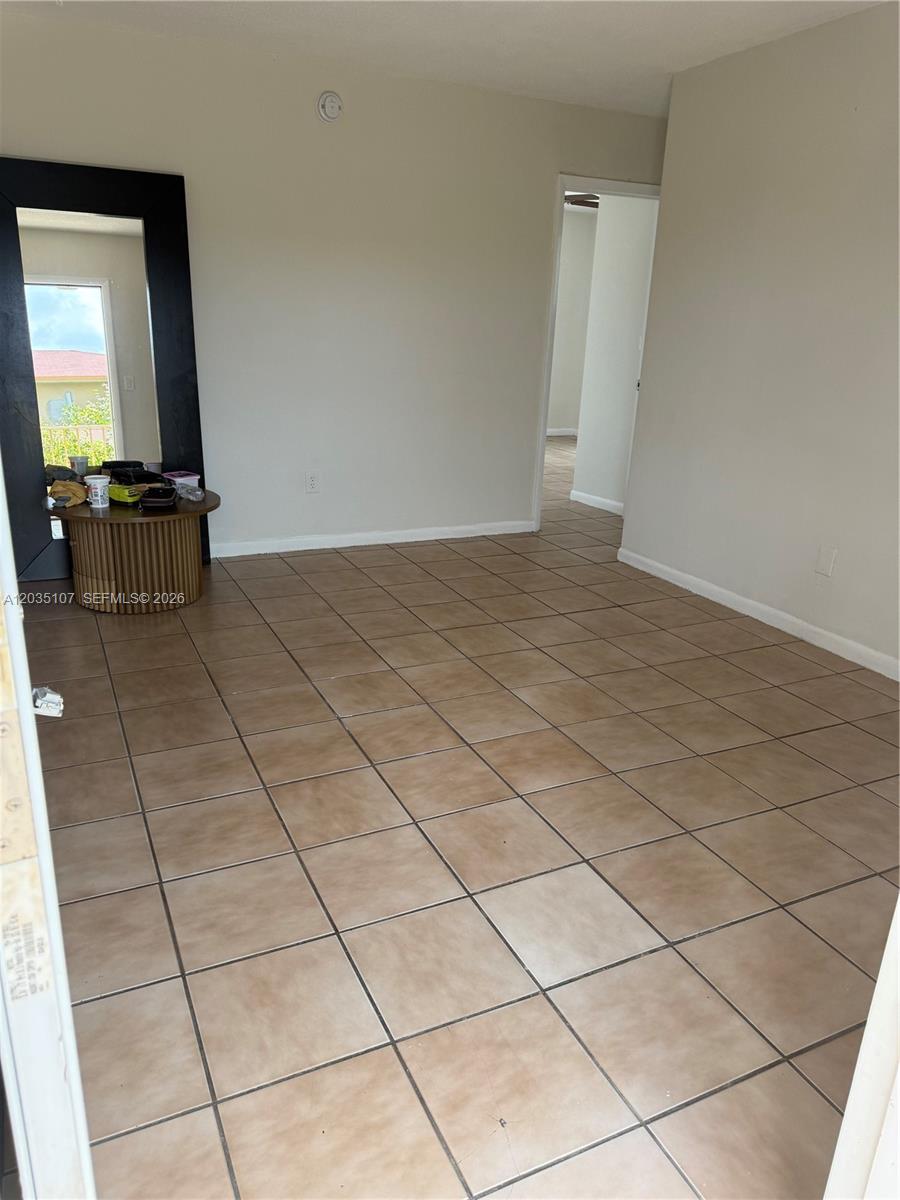 An empty room features tan floor tiles, beige walls, and a large floor mirror — 166 W 8th St # 3, Hialeah FL 33010, HIALEAH, FL