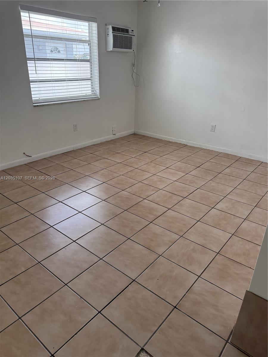 An empty room features beige tiled flooring, white walls, and a window air conditioning unit — 166 W 8th St # 3, Hialeah FL 33010, HIALEAH, FL