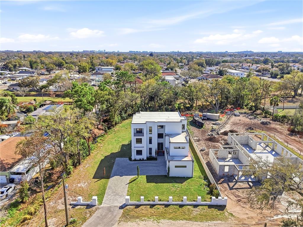 An aerial view shows a modern white multi-story house next to a concrete construction site — 7818 N HUBERT AVENUE, TAMPA, FL