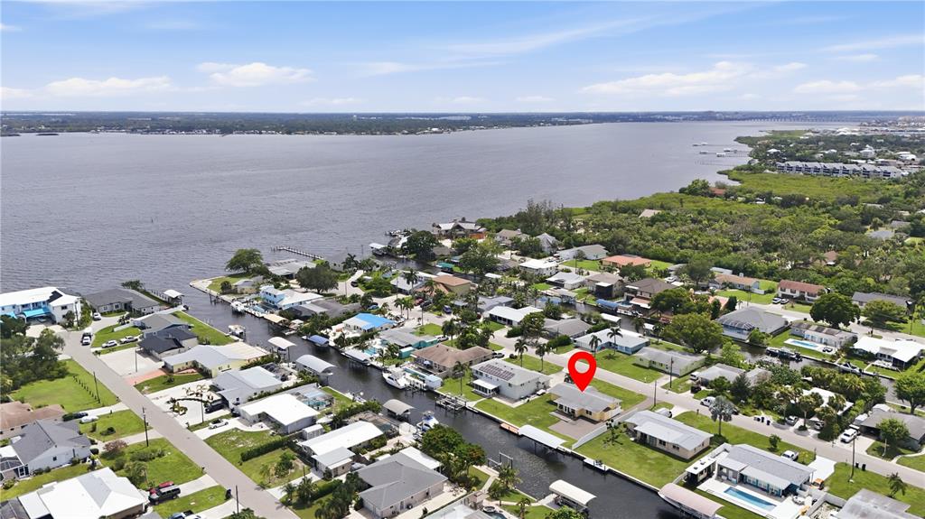 An aerial view shows a yellow waterfront house with a red location pin — 712 POINSETTIA AVENUE, ELLENTON, FL