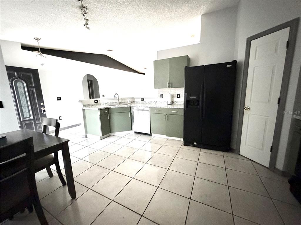A kitchen features sage green cabinets, a black refrigerator, and light-colored tile flooring — 6762 POMEROY CIRCLE, ORLANDO, FL