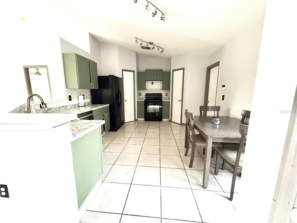 A kitchen and dining area with light tile floors, green cabinets, and black appliances — 6762 POMEROY CIRCLE, ORLANDO, FL