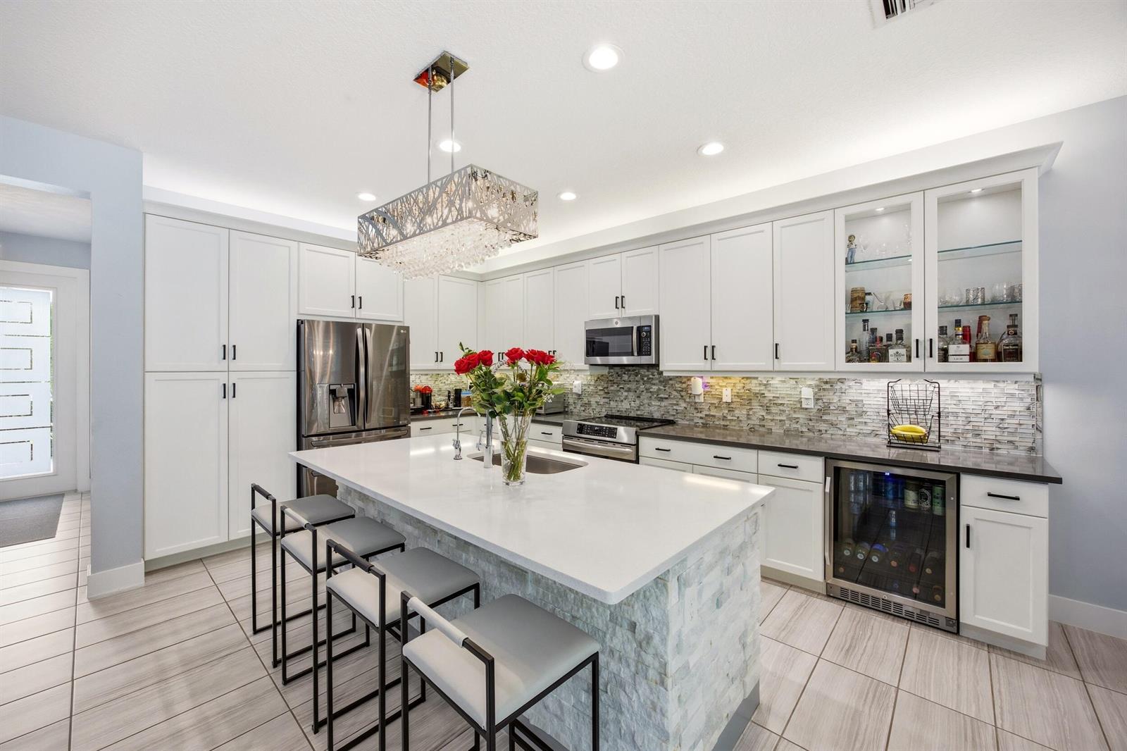 A modern kitchen features white cabinetry, a stone-faced island with bar seating, and tile flooring — 15388 Destiny Drive, Delray Beach FL 33446, DELRAY BEACH, FL