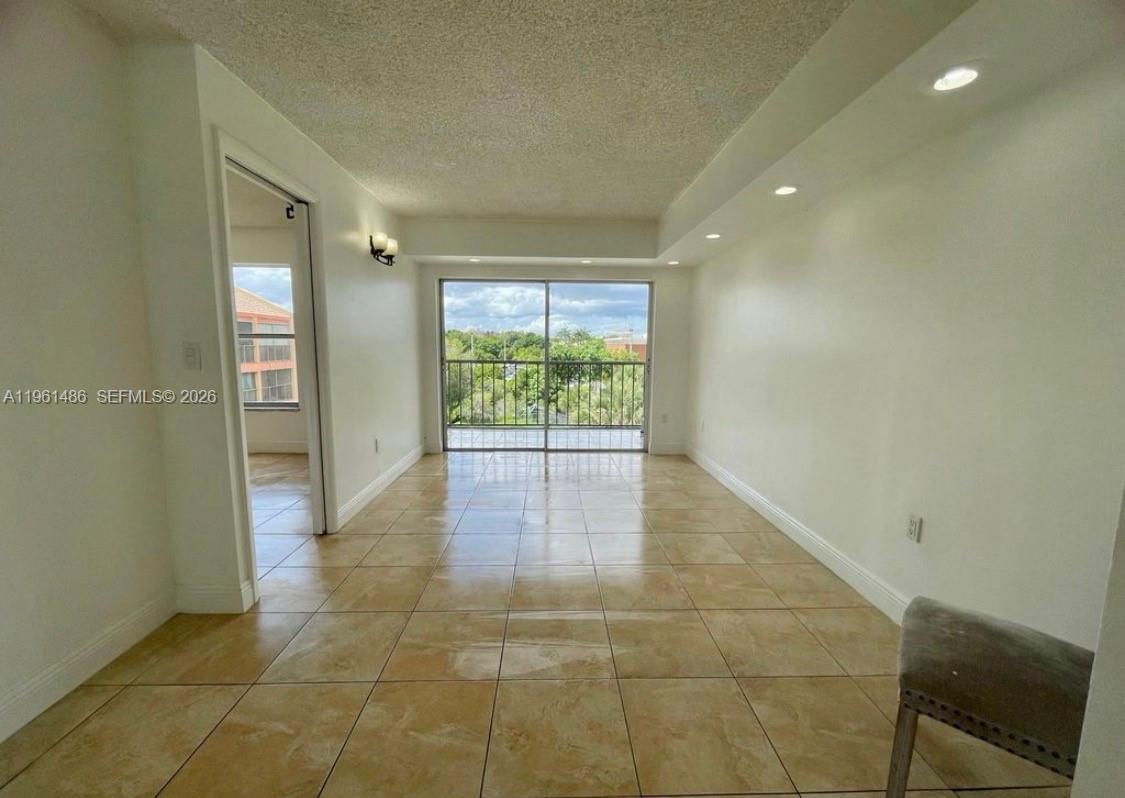 A living room with beige tile flooring, white walls, recessed lighting, and a sliding glass door — 9405 W Flagler St # D403, Miami FL 33174, MIAMI, FL