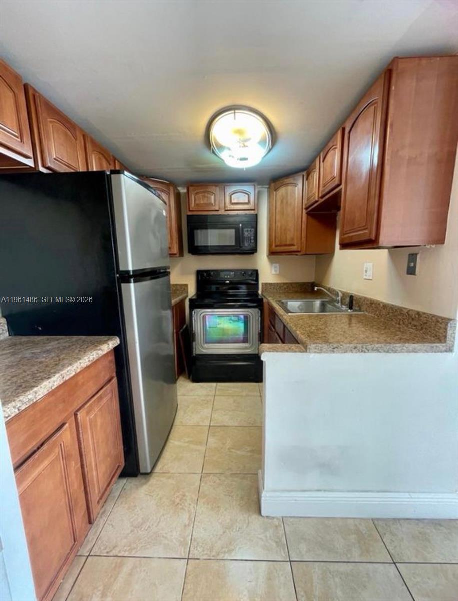 A galley-style kitchen features wood cabinets, granite countertops, tile flooring, and stainless steel appliances — 9405 W Flagler St # D403, Miami FL 33174, MIAMI, FL