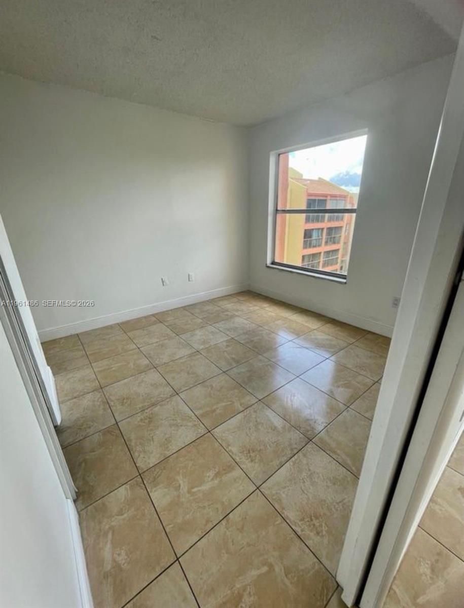 An empty room features light-colored tile flooring, white walls, and a window overlooking a building — 9405 W Flagler St # D403, Miami FL 33174, MIAMI, FL
