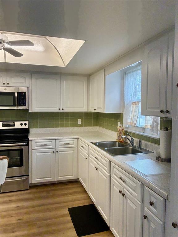 A kitchen features white cabinets, green tile backsplash, stainless steel appliances, and wood-look flooring — 1674 S LAKE AVENUE UNIT 6, CLEARWATER, FL