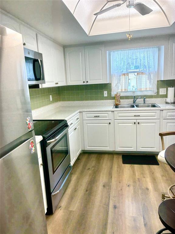 A kitchen features white cabinets, green tile backsplash, stainless steel appliances, and wood-look flooring — 1674 S LAKE AVENUE UNIT 6, CLEARWATER, FL