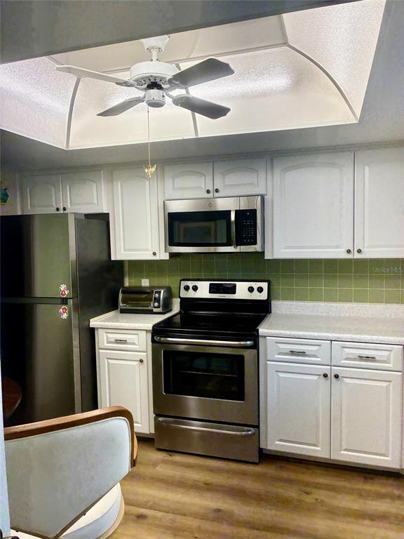 A kitchen features white cabinets, stainless steel appliances, and a green tiled backsplash — 1674 S LAKE AVENUE UNIT 6, CLEARWATER, FL