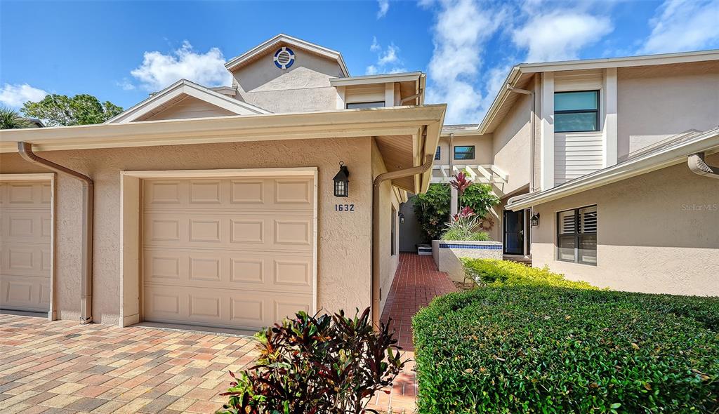 The exterior of a tan house features a garage, a brick walkway, and a landscaped hedge — 1632 STARLING DRIVE UNIT 101, SARASOTA, FL