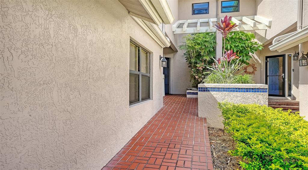 A brick walkway leads to a home entrance with a tiled planter and lush landscaping — 1632 STARLING DRIVE UNIT 101, SARASOTA, FL