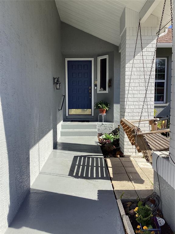 A covered front porch features a blue door, a porch swing, and gray painted concrete — 6426 DRAKE COURT, NEW PORT RICHEY, FL